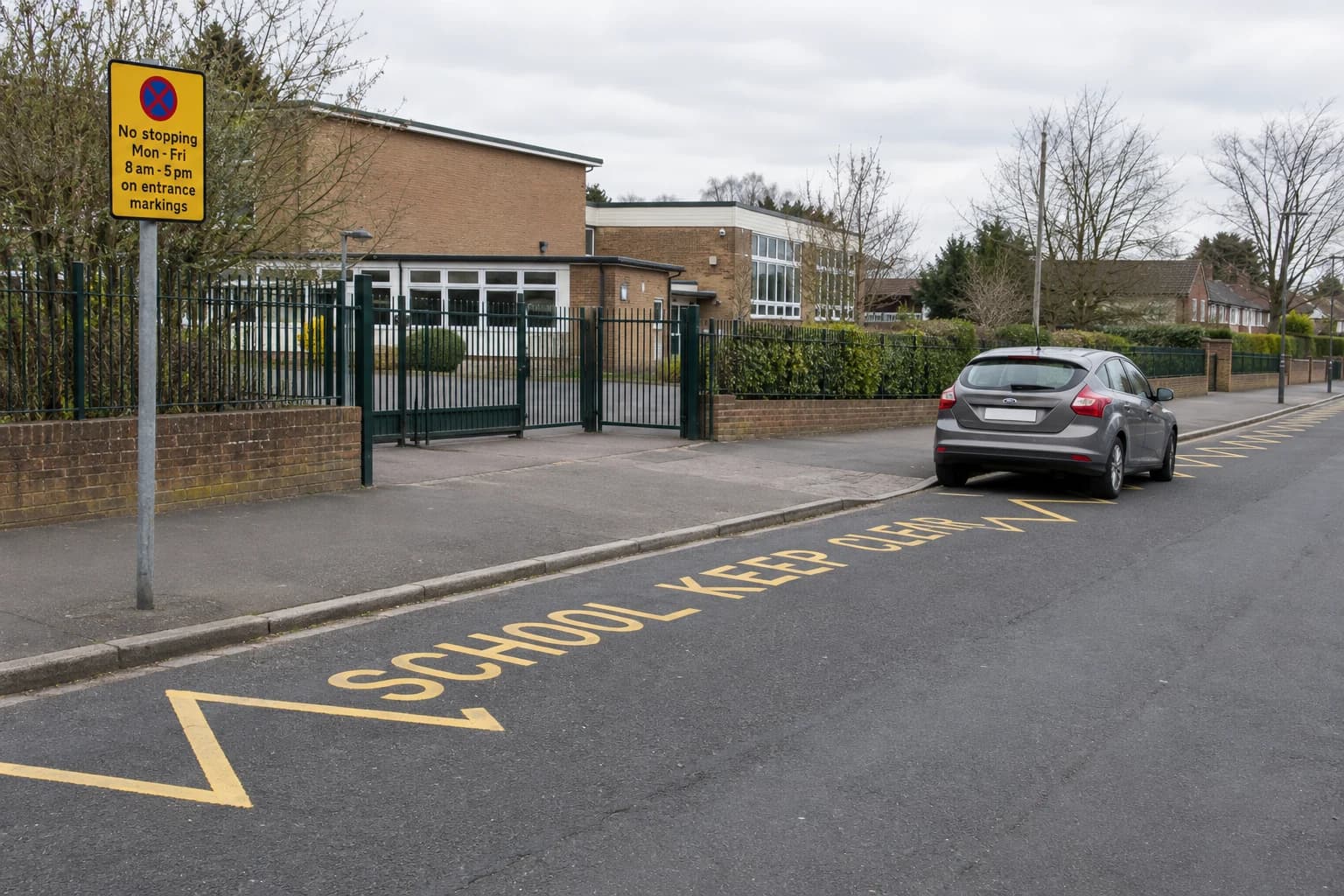 Car beside yellow SCHOOL KEEP CLEAR zigzags outside a school entrance with an upright restrictions sign.