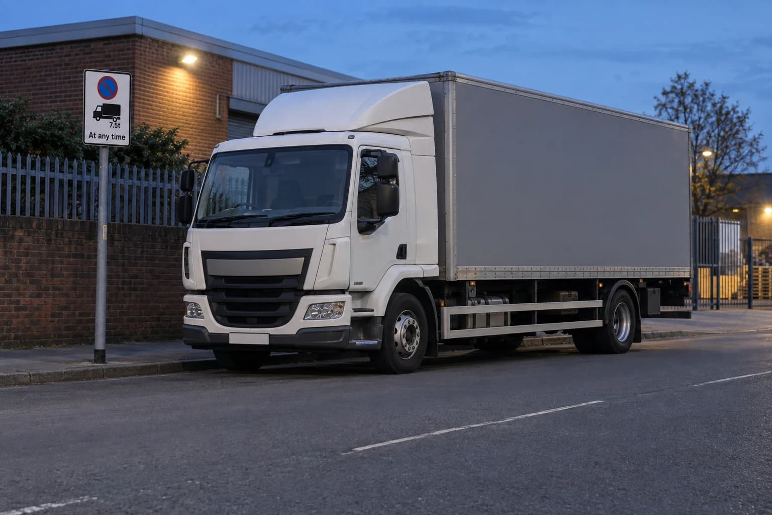 Goods lorry waiting beside a British road at blue hour near a goods-vehicle waiting plate.